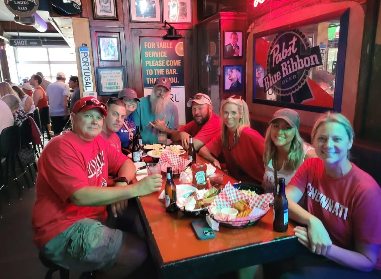 A group of friends sharing wings and fries at a table near the Shot Corner sign