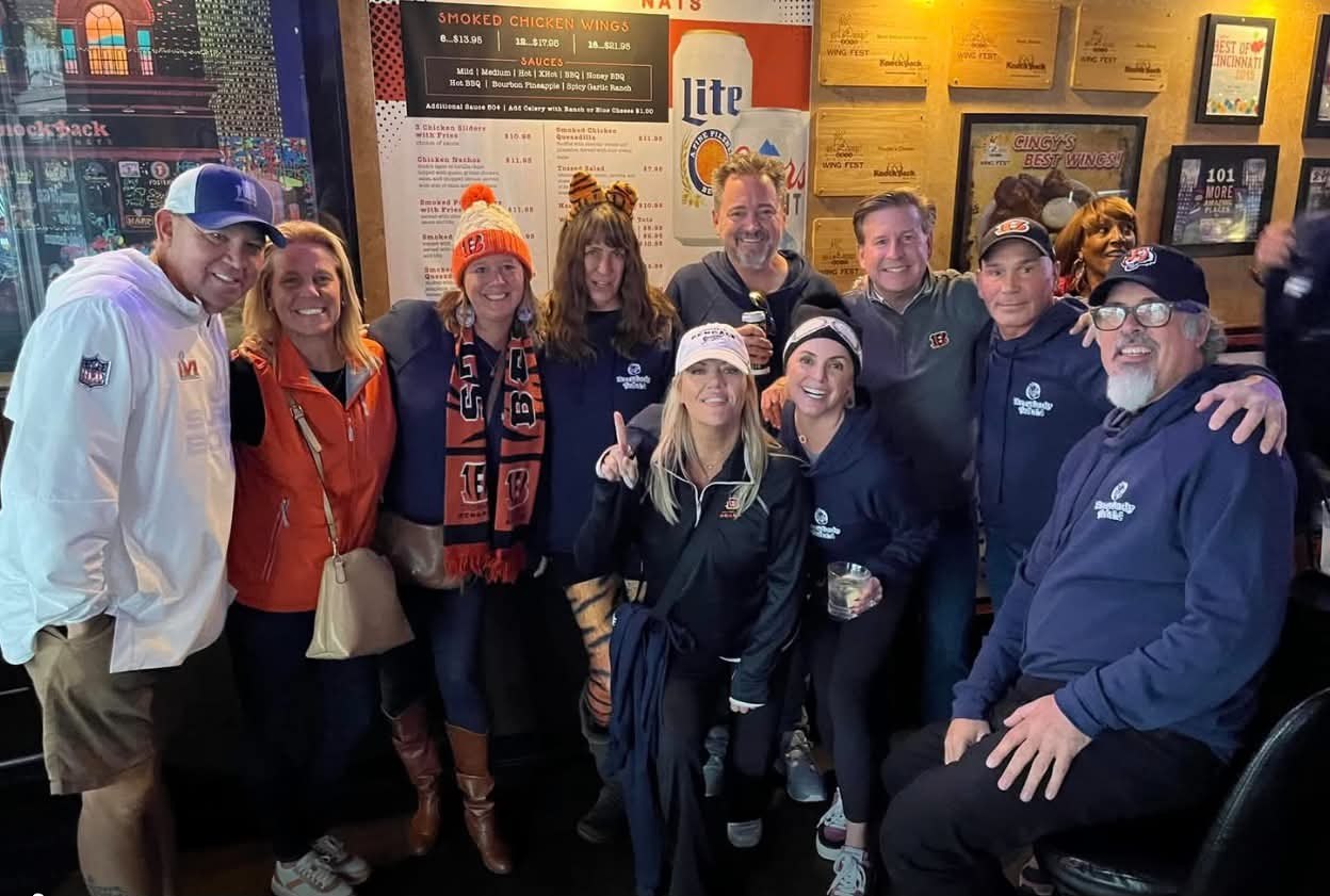 A group of friends posing in front of Knockback Nat's wing menu and Best of Cincinnati awards